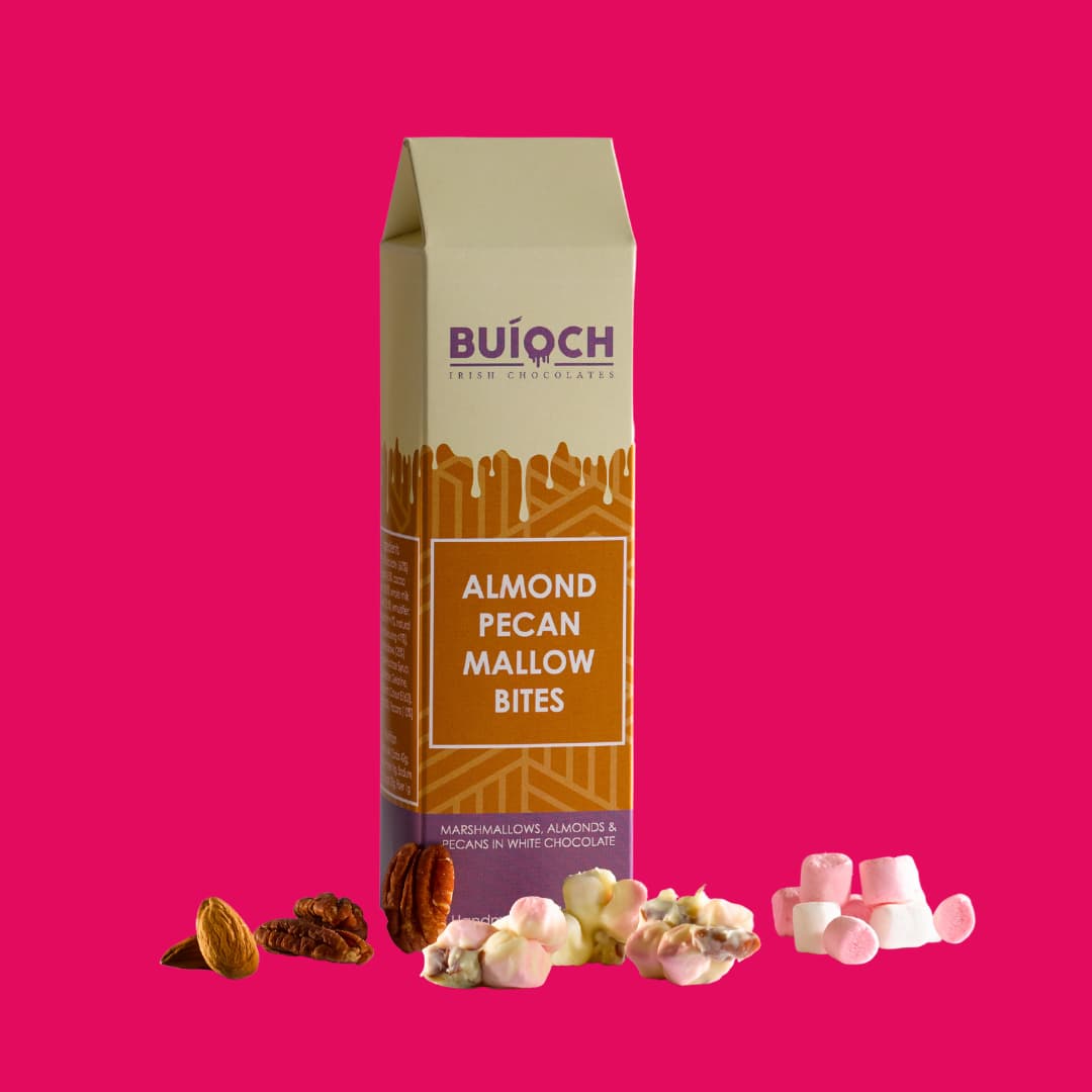 
                  
                    Almond Pecan Mallow Bites - Marshmallows, Almonds and Pecans in White Chocolate. Handamde by Buíoch Irish Chocolates. Packaging, Bites and Ingredients on a Pink Background.
                  
                