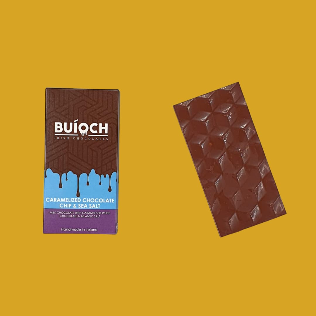 Caramelised Chocolate Chip and Sea Salt Milk Chocolate Bar - Milk Chocolate bar with caramelised white chocolate chips and atlantic sea salt. Handamde by Buíoch Irish Chocolates. Packaging and bar on a gold background.