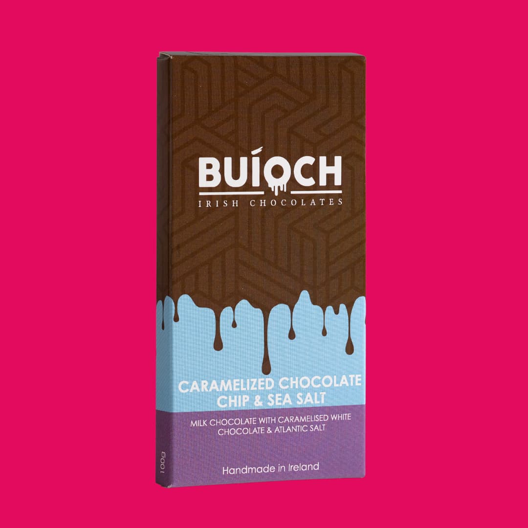Caramelised Chocolate Chip and Sea Salt Milk Chocolate Bar - Milk Chocolate bar with caramelised white chocolate chips and atlantic sea salt. Handamde by Buíoch Irish Chocolates. Packaging on a pink background.