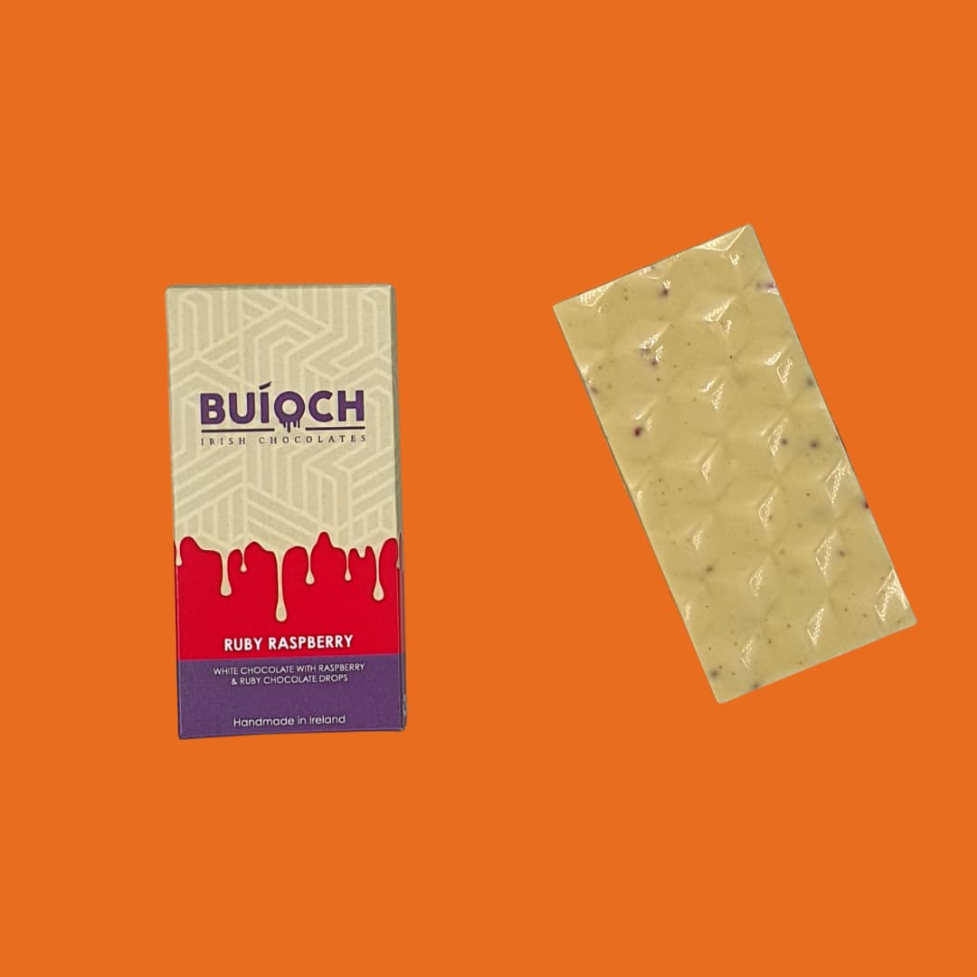 Ruby Raspberry Bar - White chocolate with raspberry and ruby chocolate drops. Handmade by Buíoch Irish Chocolates. Packaging and bar on an orange background.