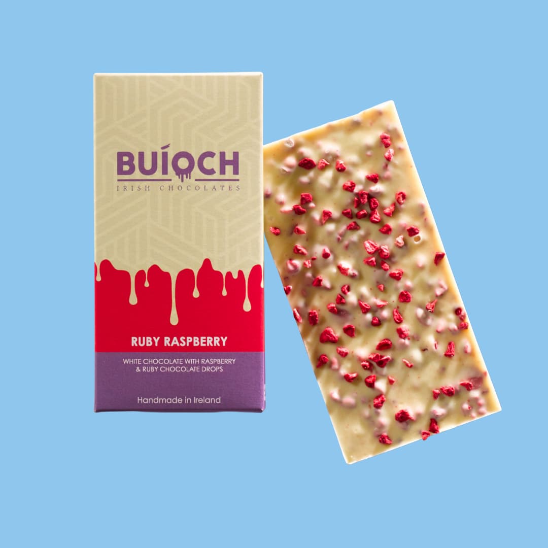 Ruby Raspberry Bar - White chocolate with raspberry and ruby chocolate drops. Handmade by Buíoch Irish Chocolates. Packaging and bar on a blue background.