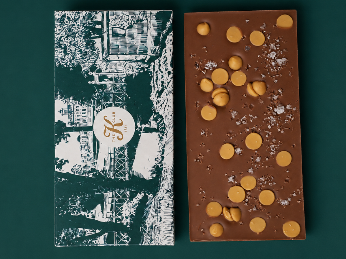 Chocolate bar topped with caramelised chocolate chips beside a green illustrated hotel-branded sleeve