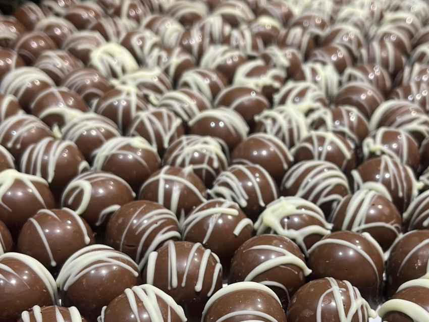 Rows of round chocolate bonbons decorated with white chocolate drizzle