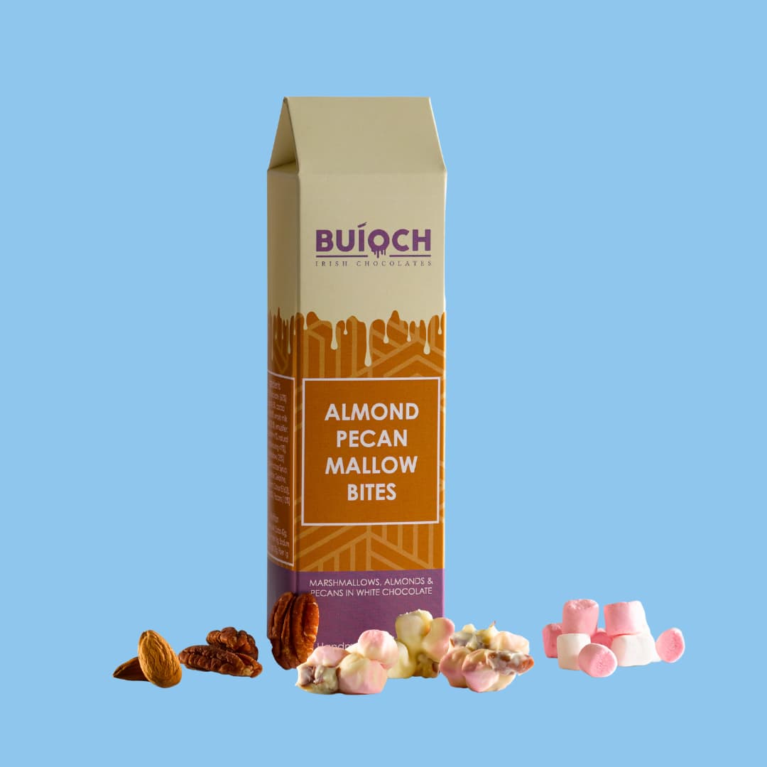 
                  
                    Almond Pecan Mallow Bites in White Chocolate. Handmade by Buíoch Irish Chocolates. Packaging on a sky blue Background.
                  
                