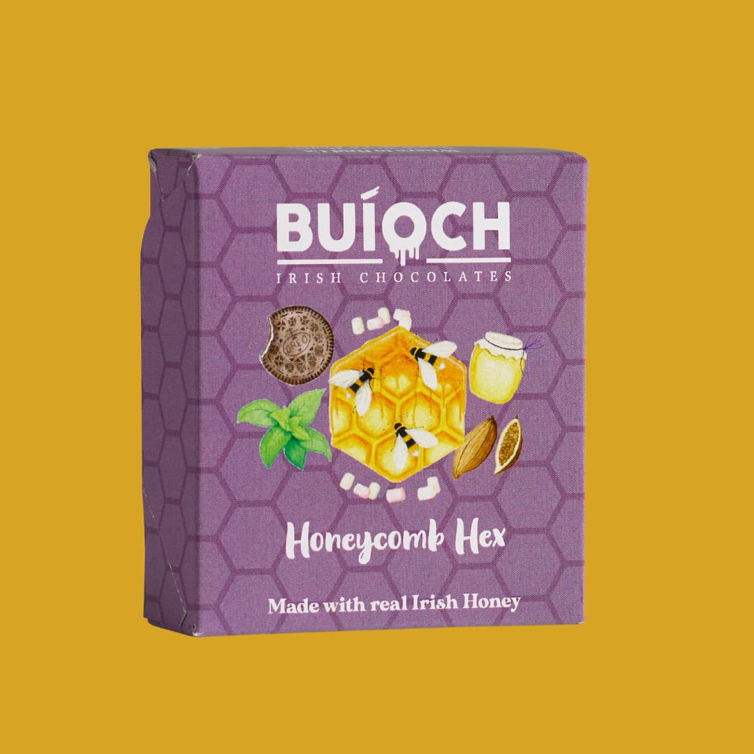 
                  
                    White Chocolate Cookies & Cream Honeycomb Hex - Packaging on a gold background. Handamde by Buíoch Irish Chocolates.
                  
                