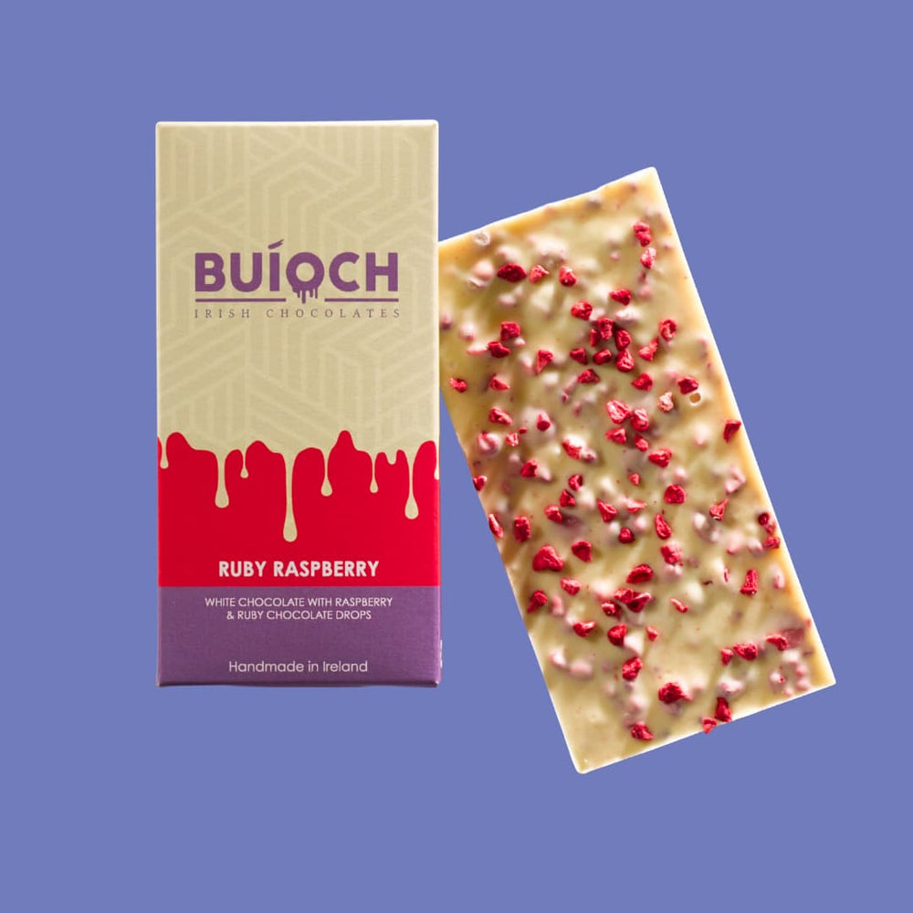 
                  
                    Ruby Raspberry Bar - White chocolate with raspberry and ruby chocolate drops. Handmade by Buíoch Irish Chocolates. Packaging and bar on a blue background.
                  
                