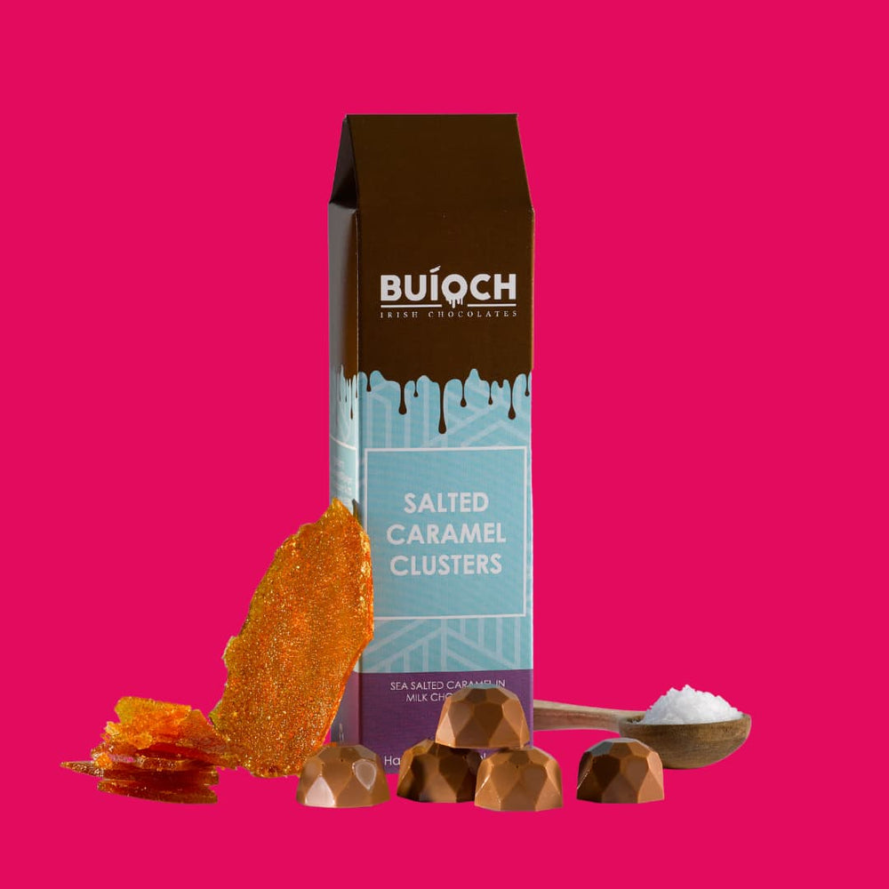 Salted Caramel Clusters - Sea salted caramel in milk chocolate. Handmade by Buíoch Irish Chocolates. Packaging, clusters and ingredients on a pink background